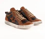 Zapatilla de cuero vacuno con diseño bicolor en marrón y negro. Presenta un aplique de estrella en el lateral, detalles de costuras y perforaciones decorativas tipo brogue. Cuenta con suela de goma con efecto desgastado y cordones al tono.