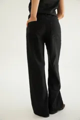 Pantalón de corte recto y tiro medio con costuras a la vista, bolsillos delanteros y traseros, y un detalle de pin de la marca en el ruedo.