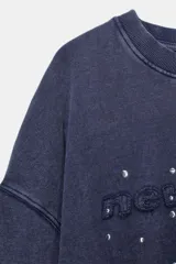 Sudadera de cuello redondo y manga larga con efecto lavado. Presenta texto bordado en el frente y aplicación de tachas decorativas. Posee puños y ruedo con acabado en rib.