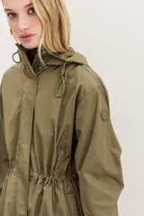 Campera impermeable negra a la rodilla de corte amplio, con cierre frontal, capucha, bolsillos y elástico en los puños. Cuenta con cordones de diseño personalizado en la cintura y la capucha, y detalles en símil cuero en bolsillos y cierre delantero.