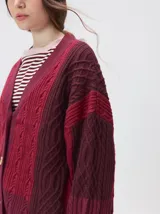 Cardigan oversize de tejido de punto grueso con diseño de bloques de color en tonos beige y marrón. Presenta cuello en V, cierre frontal con botones, mangas largas abullonadas y parches decorativos en el pecho y el hombro.