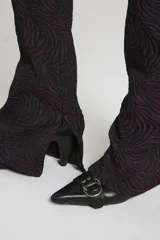 Pantalón de tiro alto con estampado abstracto en tonos borgoña y negro, con cierres invisibles en la parte inferior de la bota en los laterales y recortes verticales.
