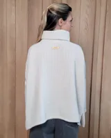 Polera de tejido suave con textura acanalada, cuello alto tipo tortuga, mangas largas y corte holgado con aberturas laterales en el ruedo.