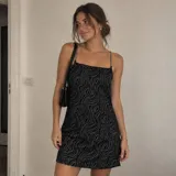 Vestido corto negro con estampado abstracto de líneas onduladas en tono plateado brillante, escote recto y tirantes finos tipo cadena metálica.