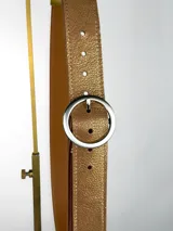 Cinturón de cuero genuino en tono tostado con acabado texturizado y detalles dorados. Presenta una hebilla circular metálica en color dorado mate.