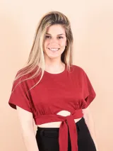 Blusa bordeaux de corte crop, con cuello redondo, mangas cortas y detalle de nudo frontal con abertura.