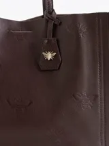 Cartera tipo shopper Jazmin Chebar modelo Honey, color negro, confeccionada en cuero vacuno suave. Cuenta con amplia capacidad, doble asa larga para el hombro y diseño grabado con abejas en bajo relieve. Incluye un tag colgante decorativo con dije metálico en forma de abeja.