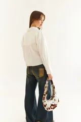 Camisa de corte boxy en color blanco, con cuello clásico, cierre frontal de botones y mangas largas con puños estructurados con tablas. Presenta costuras a contratono y detalle de frunce en la espalda.