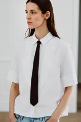 Camisa de algodón de corte recto con cuello solapa, manga corta y cierre frontal con botones ocultos. Presenta un diseño con pechera y una corbata negra extraíble a contraste.