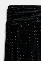 Pantalón negro de tiro bajo, confeccionado en terciopelo con pequeños puntos brillantes. Presenta cintura elástica con pliegues, caída ancha tipo baggy y puños ajustados en los tobillos.