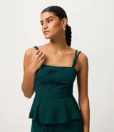 Blusa verde oscuro de viscolino con tirantes dobles ajustables mediante nudos. Presenta un corpiño estructurado con un detalle de flor en relieve en la parte delantera y smock en la espalda para un mejor ajuste. La prenda tiene un bajo peplum.