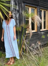 Vestido largo de lino celeste, de corte recto y holgado, con escote en V y detalles de bordado rojo en el frente.