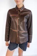 Camisa de cuero ovino con acabado gastado artesanal, corte clásico, cierre frontal con broches metálicos y mangas largas.