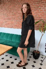 Vestido corto de lino color beige, con cuello alto, mangas cortas abullonadas con puños elásticos y volados en el pecho. Cuenta con cierre frontal de botones.