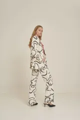 Pantalón de vestir de corte recto, con diseño estampado abstracto en blanco y negro, bolsillos laterales y cierre frontal.