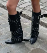 Botas de caña alta de cuero sintético negro, con punta fina y múltiples correas con hebillas y ojales plateados.