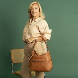 Cartera tipo hobo de cuero sintético color rojo ladrillo, con correa de hombro ajustable. Tiene cierre superior con solapa y broche magnético, bolsillo frontal con cierre, bolsillos laterales con cierre y múltiples bolsillos internos.