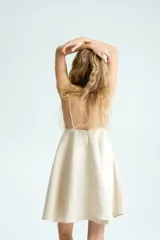 Vestido corto color beige, con escote en V pronunciado, tirantes finos ajustables, corte bajo el busto y falda acampanada con vuelo.