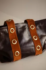 Cartera tipo tote de cuero color marrón, con detalles de cuero con pelo estampado animal print en las asas y ojales metálicos decorativos.