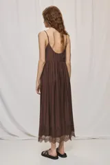 Vestido largo negro de silueta fluida, con breteles finos y escote en V con detalles de encaje. Presenta frunce bajo el busto y terminación de encaje en el ruedo.