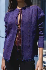 Cardigan de punto en color violeta con destellos de lurex, diseño de manga larga y cierre frontal con lazos. Presenta detalles de mostacillas en el ruedo.