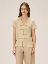 Camisa de lino, algodón y viscosa color beige con brillo dorado, escote en V, mangas cortas y cierre frontal con botones y detalles de galones decorativos estilo oriental.