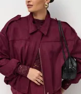 Campera bomber de gamuza sintética color bordó, con cuello clásico, cierre frontal, hombros caídos y puños ajustados.