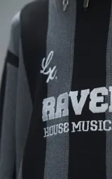 Sweater de punto con diseño a rayas verticales en negro y gris, cuello redondo y mangas largas. Presenta un estampado gráfico frontal con estilo deportivo retro que incluye el texto 'Ravers' y el número '90'. Cuenta con terminaciones en punto rib en cuello, puños y ruedo.