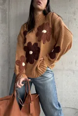 Sweater de punto grueso color camel, con diseño de flores grandes aplicadas en tonos marrones y centro crema. Presenta cuello redondo alto, mangas largas con hombros caídos y terminaciones acanaladas.