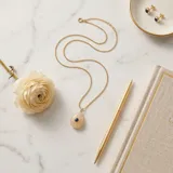 Collar de acero con baño de oro, compuesto por una cadena fina y un dije en forma de lágrima de cuarzo rosa natural con una circonia azul engastada en el centro.