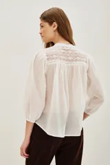 Camisa de algodón color celeste, con cuello mao, cierre frontal parcial con botones y detalles de encaje en los hombros y canesú. Presenta mangas largas abullonadas con puños elásticos.