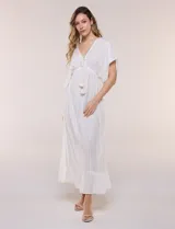 Vestido largo blanco confeccionado en viscosa con hilos de lurex, escote en V profundo con lazo y borlas, mangas kimono y falda fluida con volados en el ruedo.