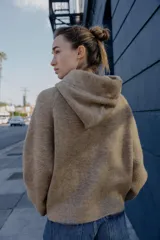 Chaqueta de punto con capucha, manga larga y cierre frontal con cremallera. Presenta un diseño en color beige con un lazo decorativo a contraste en color marrón oscuro en la zona del cuello.