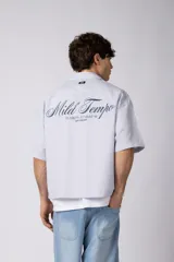 Camisa de manga corta de popelina rayada, con calce boxy y bordado sutil en el pecho. Presenta cierre frontal con botones y diseño abierto.