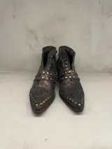 Bota corta de cuero color gris oscuro con detalles cobrizos y tachas doradas. Tiene cierre lateral y taco de 5 cm.