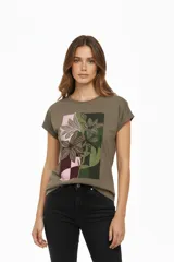 Remera de algodón color verde militar, manga corta con puños doblados y cuello redondo. Presenta un estampado frontal con motivos florales y un fondo con patrón de cuadros en tonos rosados, marrones y verdes.