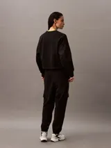Buzo Calvin Klein de felpa francesa color negro, de corte holgado y diseño con cuello redondo. Cuenta con mangas largas, puños y dobladillo acanalados, y lleva el logo retro de la marca bordado discretamente en el pecho.
