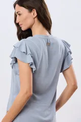 Camisa lisa de lino y viscosa color celeste, de manga corta con volados superpuestos y cuello mao con pequeña abertura y botón en la espalda.