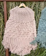 Poncho de lana merino color marfil, tejido a mano con diseño de puntos en relieve y largos flecos en los bordes.
