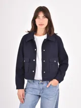 Chaqueta corta de paño en color azul oscuro, con cuello camisero, cierre frontal con botones metálicos dorados y dos bolsillos frontales con solapa.