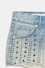 Shorts de denim de tiro medio con cinco bolsillos, detalles de rotos y aplicación de tachas metálicas en la parte delantera. El bajo presenta un acabado deshilachado sin costuras.