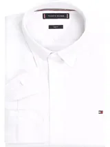 Camisa blanca de corte slim fit, confeccionada en tejido dobby de puro algodón con tecnología Flex que ofrece elasticidad en cuatro direcciones. Tiene cuello abotonado, logo de Tommy Hilfiger bordado en el pecho y cinta distintiva en el interior del cuello.