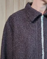 Chaqueta de textura bouclé en color bordó, con corte oversize, cuello camisero, cierre frontal y bolsillos laterales.