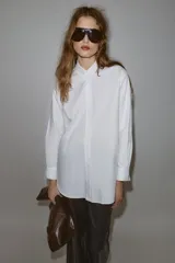 Camisa de corte oversize con cuello solapa, manga larga con puños y bajo asimétrico. Cierre frontal con botones.