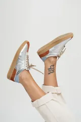 Zapatillas deportivas de cuero color beige con detalles en naranja y suela marrón.