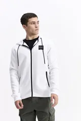 Campera con capucha de algodón y poliéster, color blanco, con cierre frontal negro y cordones negros en la capucha. Presenta un pequeño parche cuadrado negro con texto blanco en el pecho izquierdo y cierres negros en los bolsillos laterales.