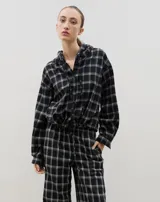 Camisa de manga larga con capucha, confeccionada en tejido liviano con estampado a cuadros. Presenta cierre frontal con botones y lazo regulable en la cintura.