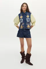 Chaleco de denim azul oscuro con cuello clásico y bordados florales en tonos amarillos, blancos y celestes en la parte delantera.