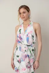 Vestido midi de gasa blanca con estampado floral en tonos rosados, azules y verdes. Presenta escote cruzado, espalda estilo halter, detalle de volados en la falda y corte irregular.