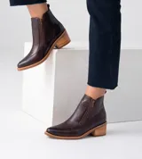 Bota corta de cuero vacuno color negro, con diseño combinado de cuero liso y cuero con textura de reptil en el empeine. Presenta punta fina, taco cuadrado de 6 cm y doble cierre lateral.